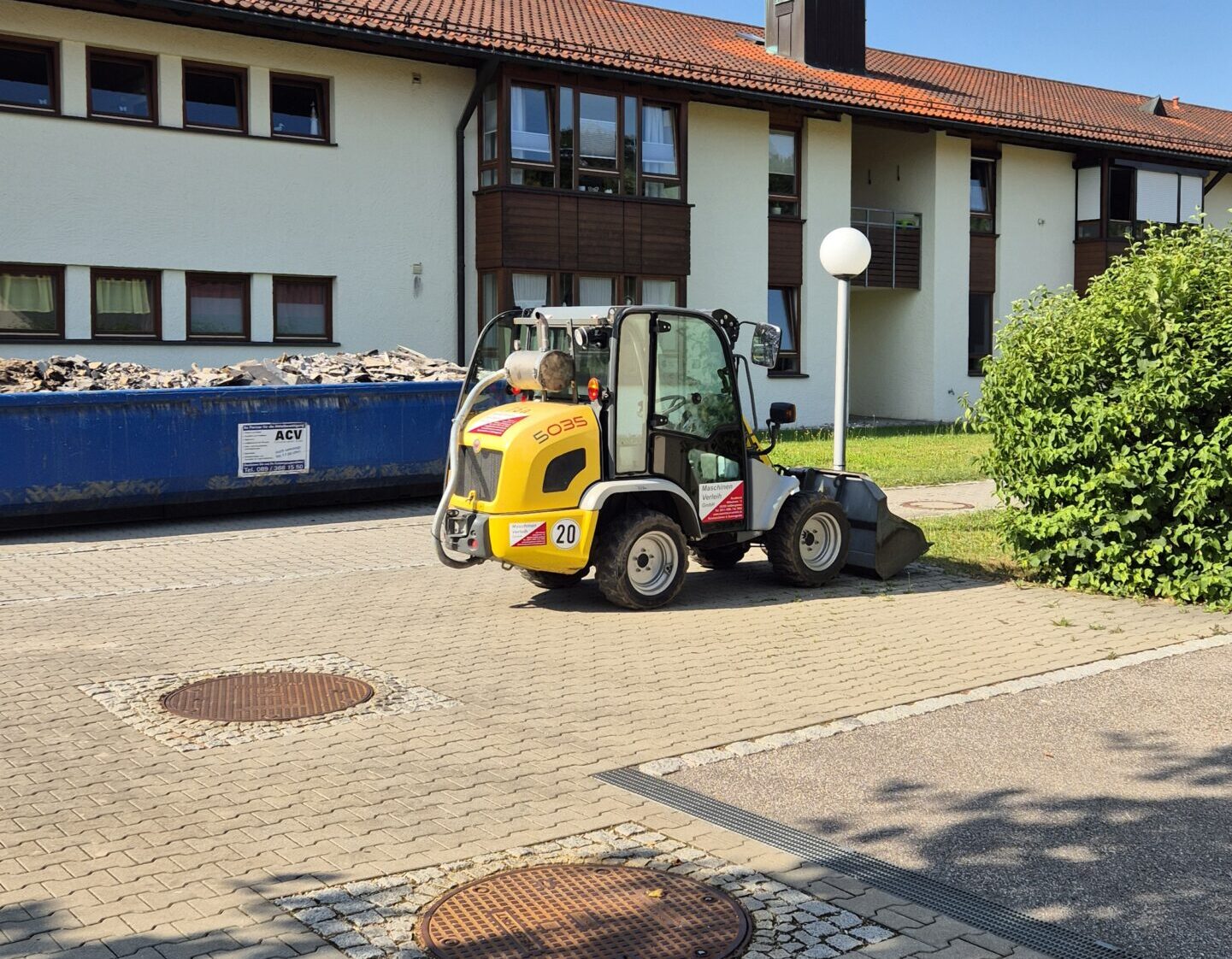 Der Radlader steht auf einem Parkplatz neben einem Bauschuttcontainer