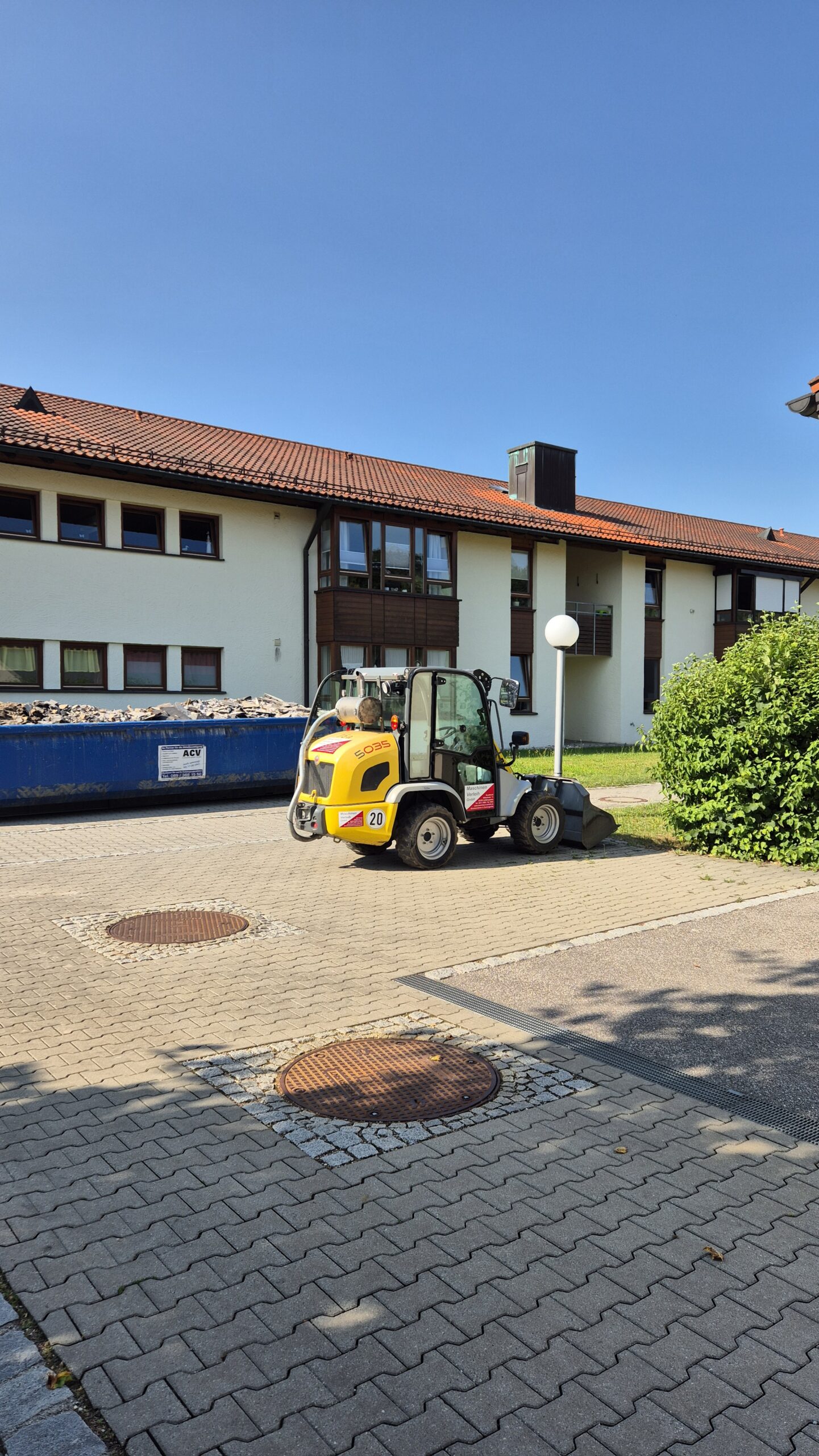 Der Radlader steht auf einem Parkplatz neben einem Bauschuttcontainer