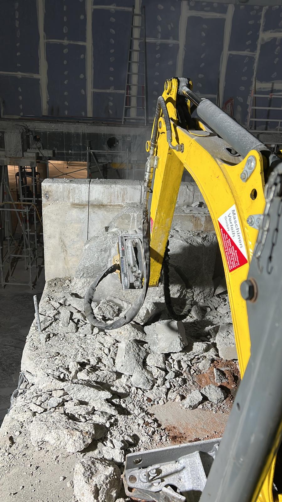 Der Elektrobagger bricht mit dem Abbruchhammer eine Betonwand ab.