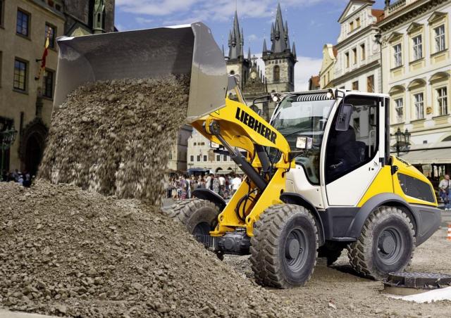 Der Radlader in der Stadt beim Auskippen mit hochgehobener Schaufel von Kies auf einen Kieshaufen.