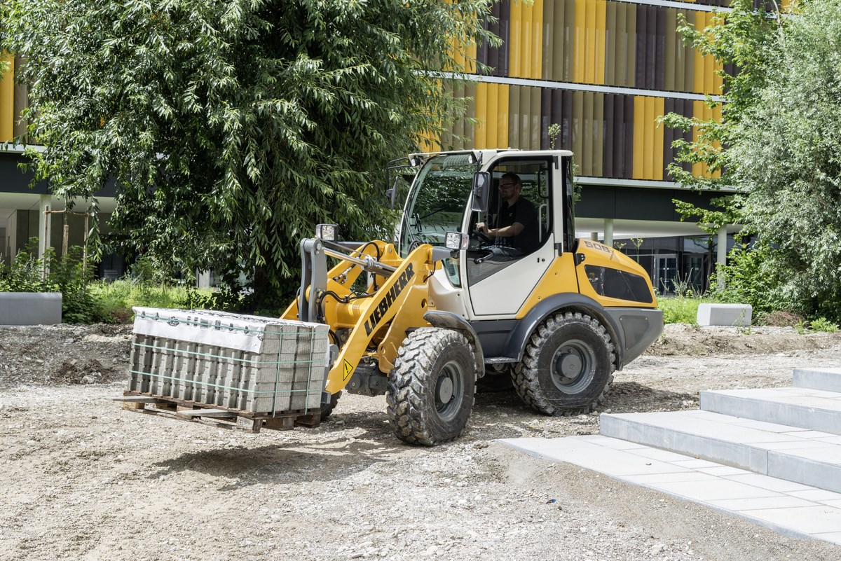 Der Radlader in einem Garten beim Verfahren einer Pflasterpalette mit der Staplergabel
