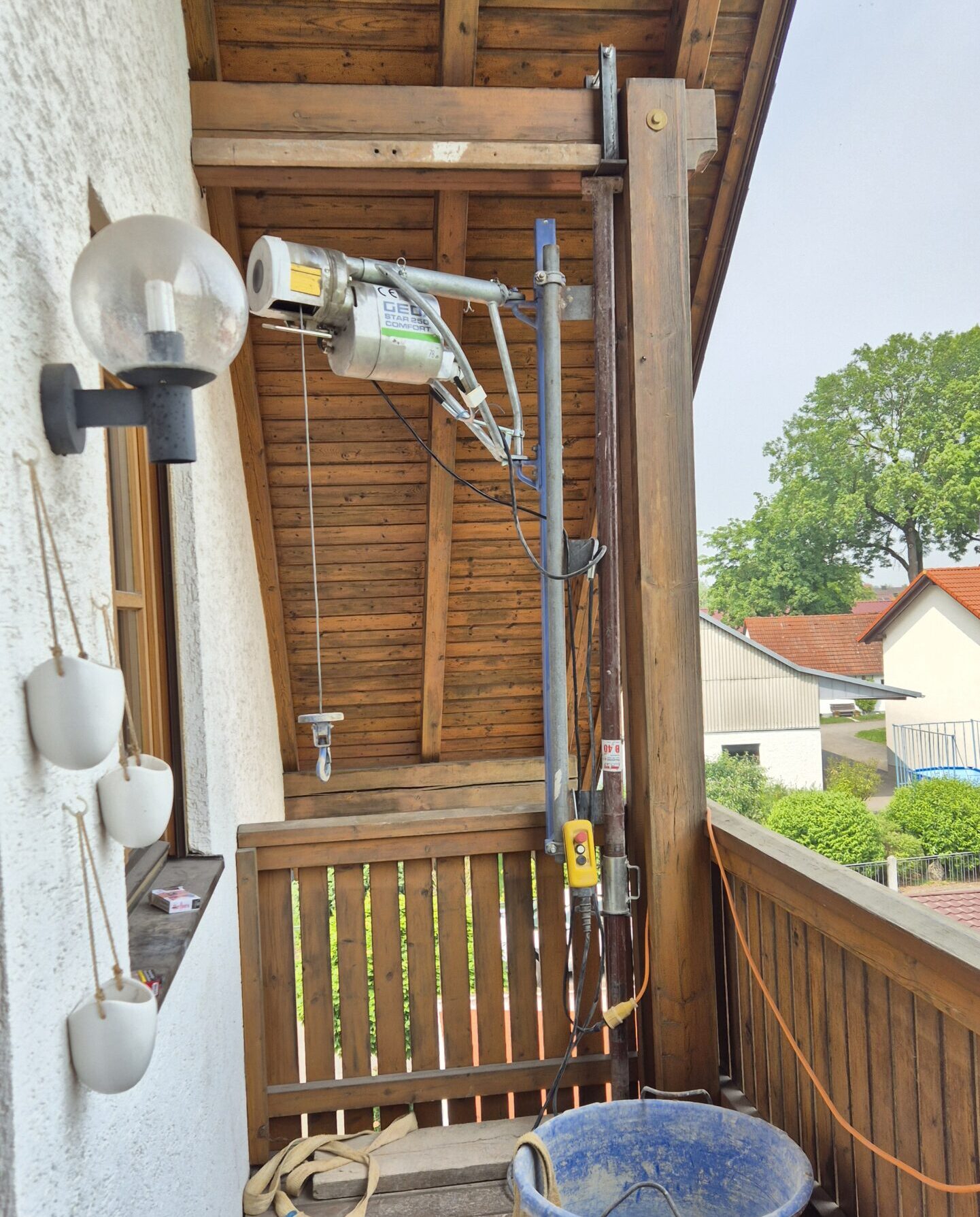 Die Seilwinde ist mit der Baustütze auf dem Balkon zwischen Balkonboden und Holzbalken an der Decke geklemmt.