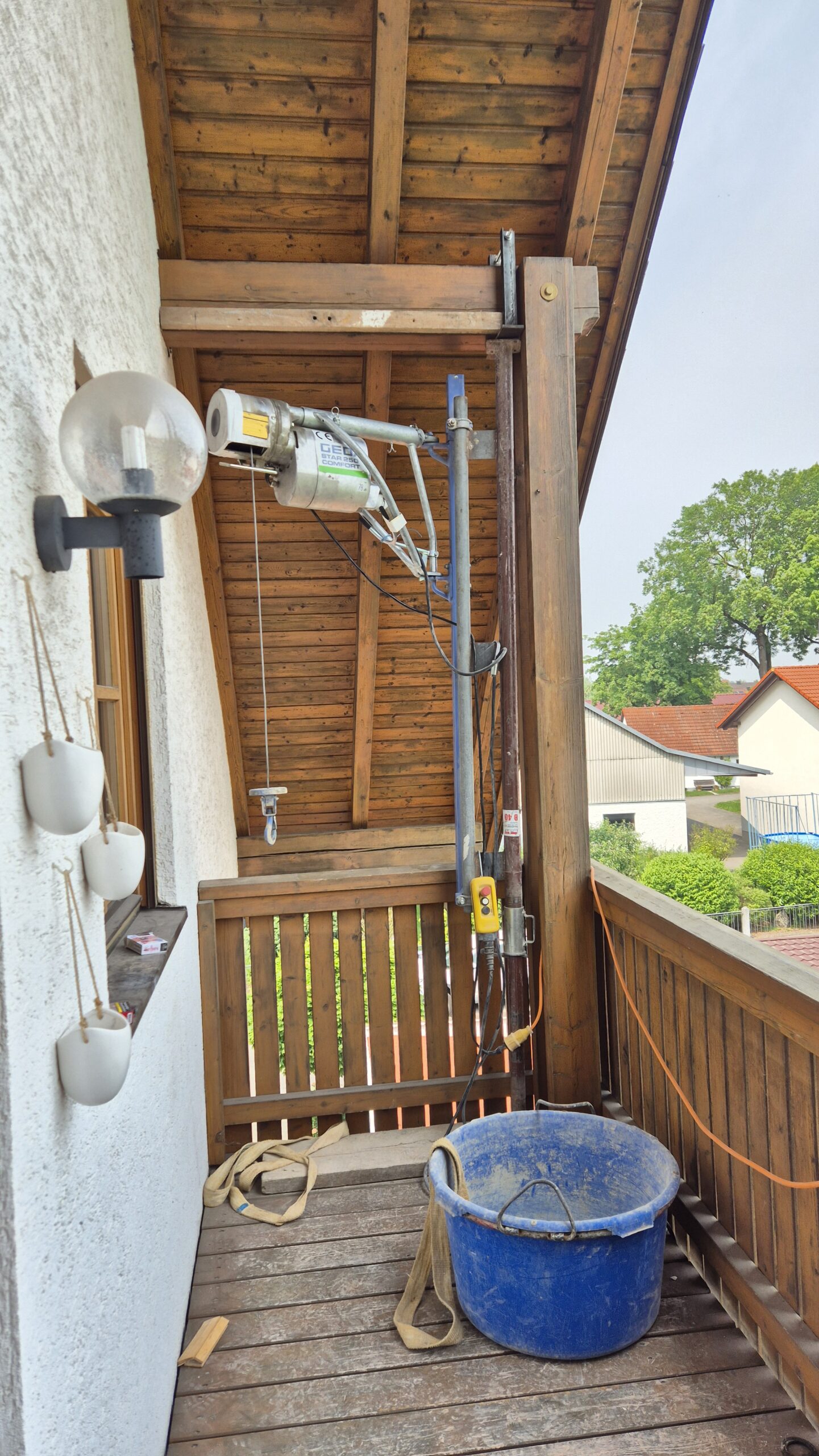 Die Seilwinde ist mit der Baustütze auf dem Balkon zwischen Balkonboden und Holzbalken an der Decke geklemmt.