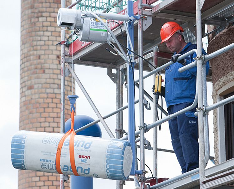 Der Seilaufzug befestigt am Gerüst beim Heben einer Dämmungsrolle