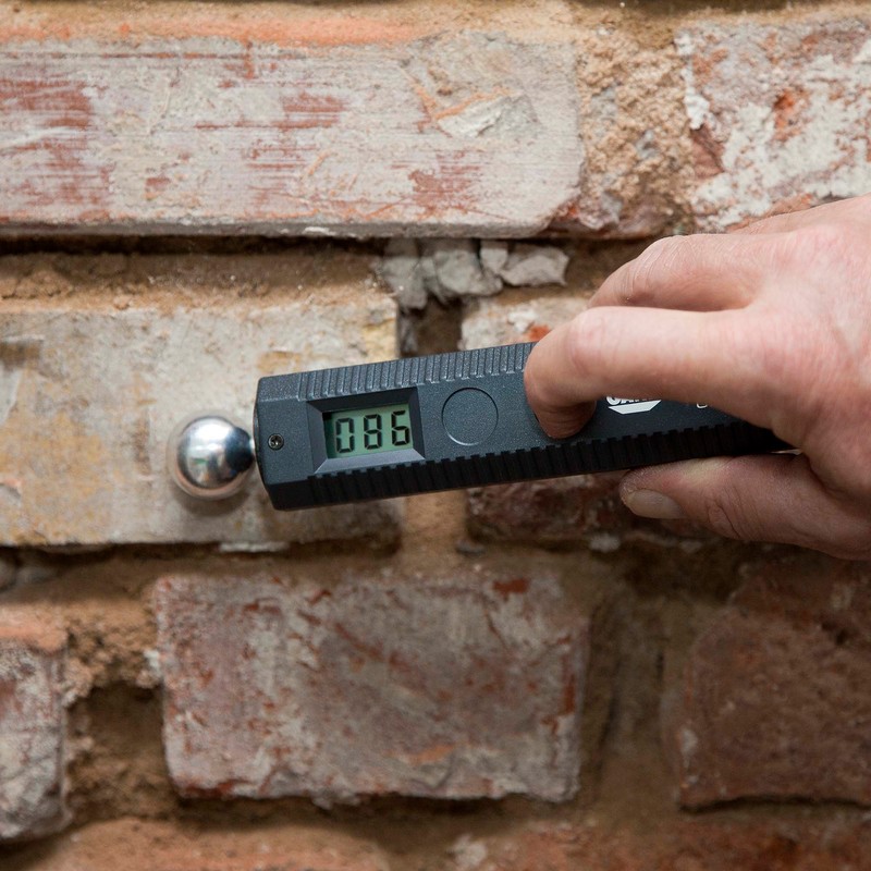Das Feuchtemessgerät wird an eine Ziegelwand gehalten.